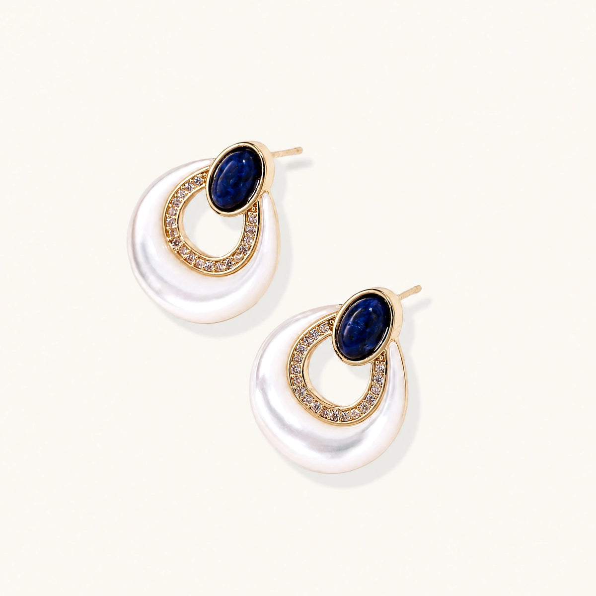 Gold plated stud earrings with an oval lapis lazuli top, CZ-lined teardrop loop and white MOP crescent on a cream background.