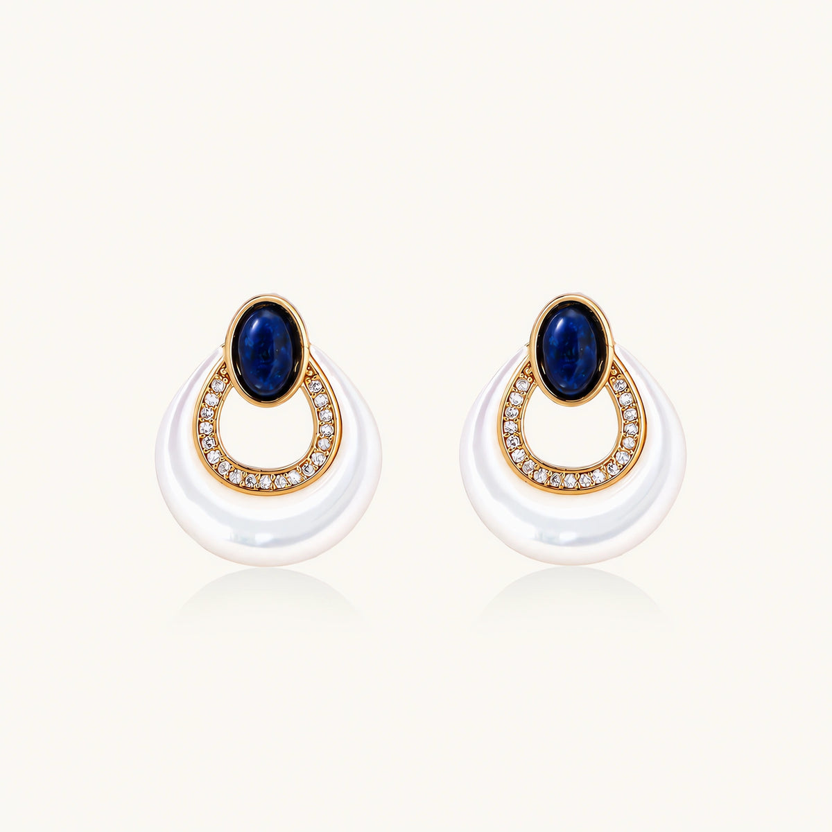 Gold plated stud earrings with an oval lapis lazuli top, CZ-lined teardrop loop and white MOP crescent on a cream background.