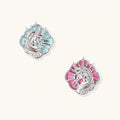 Silver unicorn stud earrings with pastel blue and pink enamel stones in sunburst prong settings on cream background