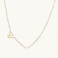 Dainty 14K gold plated stainless steel necklace with an open heart charm and a single round white bead on a cream background.