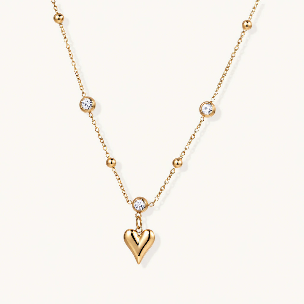Delicate gold-plated necklace with bezel-set crystals and small heart pendant on beige background