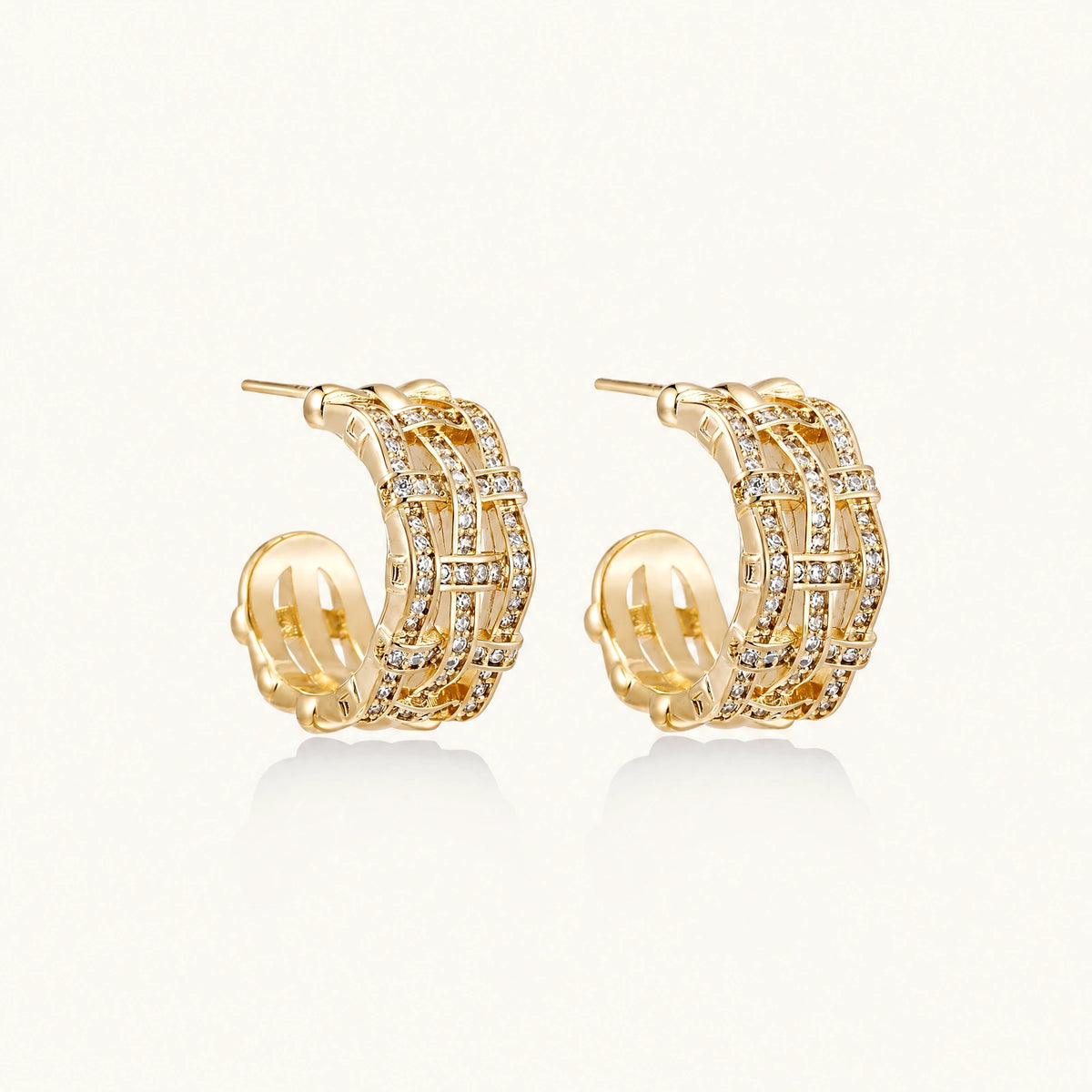 Gold-plated geometric hoop earrings with basket-weave lattice design and pavé crystal accents on cream background