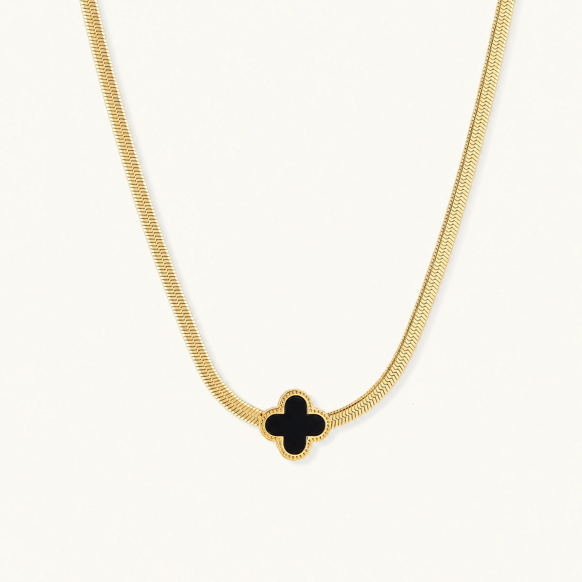 Dainty 18K gold-plated herringbone chain necklace with black enamel quatrefoil clover pendant on white background