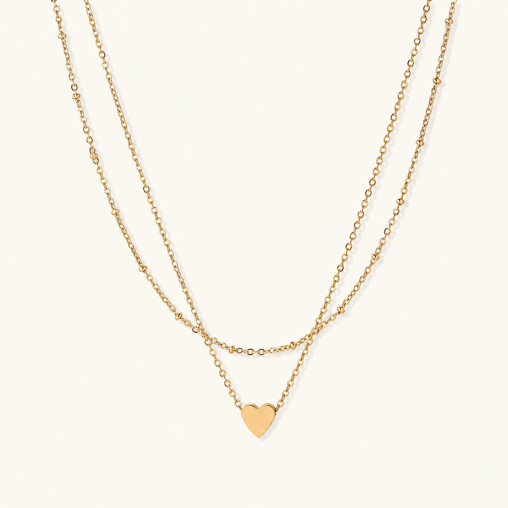 Delicate double-chain gold necklace with tiny heart pendant on cream background