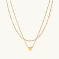 Delicate double-chain gold necklace with tiny heart pendant on cream background
