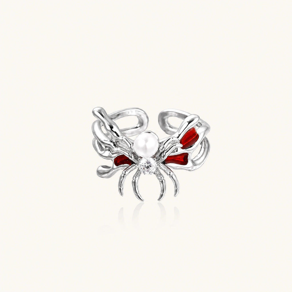 Silver-tone spider ring with red drip wings, a white bead and a round zirconia center on an open adjustable band.