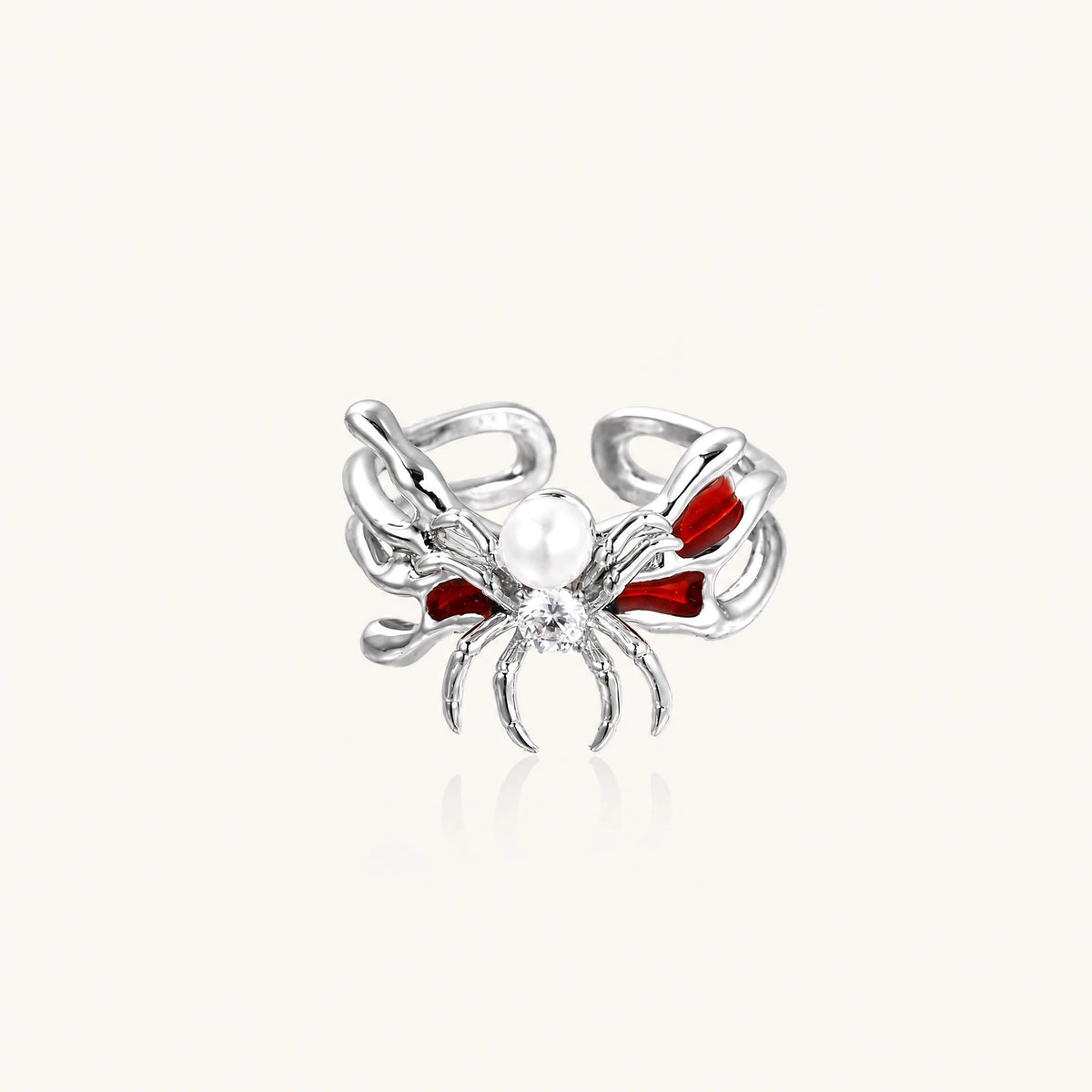 Silver-tone spider ring with red drip wings, a white bead and a round zirconia center on an open adjustable band.