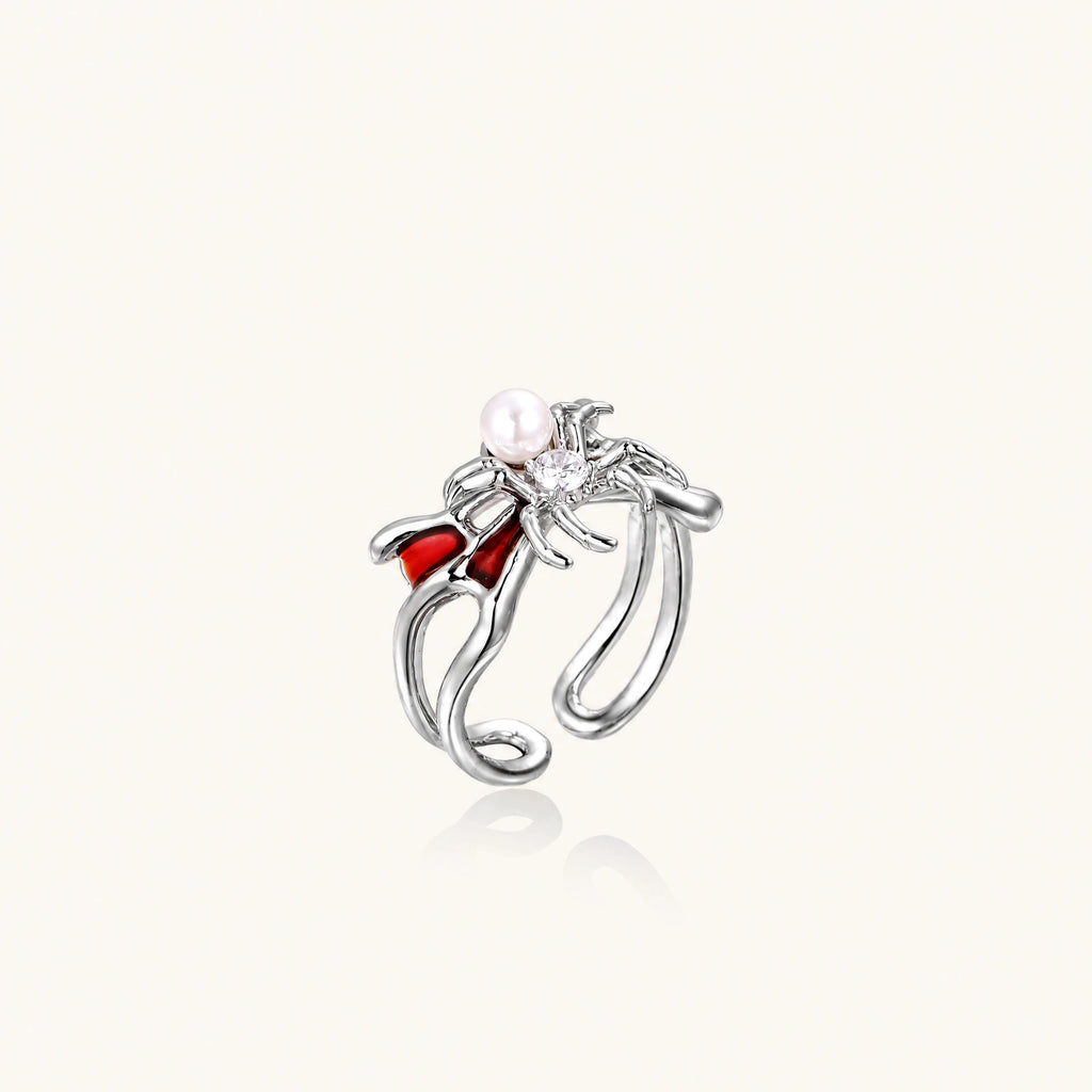 Silver-tone spider ring with red drip wings, a white bead and a round zirconia center on an open adjustable band.