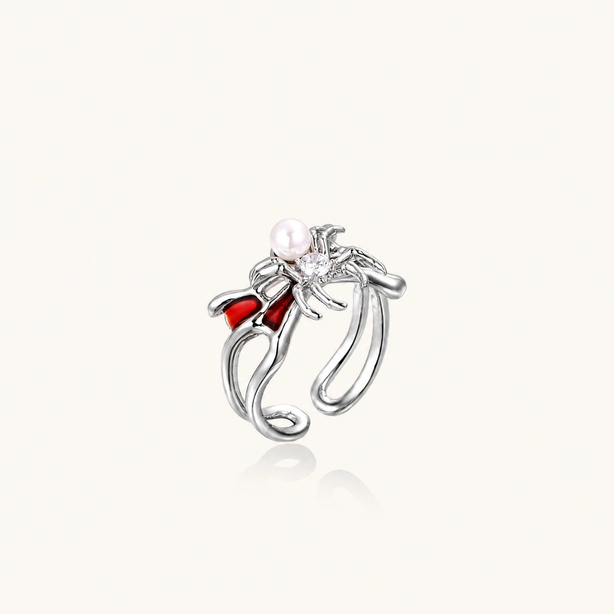 Silver-tone spider ring with red drip wings, a white bead and a round zirconia center on an open adjustable band.