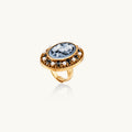 Gold-plated ring with oval blue floral cameo, pearl accents, and black enamel detailing on white background.