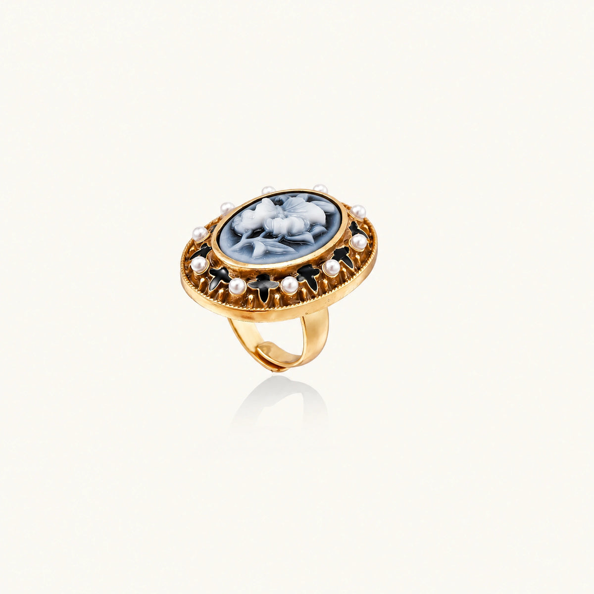 Gold-plated ring with oval blue floral cameo, pearl accents, and black enamel detailing on white background.