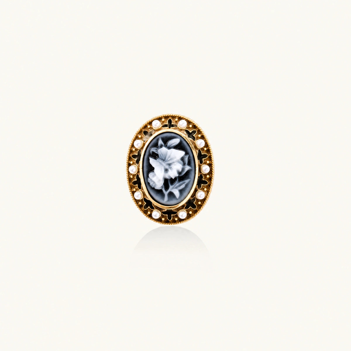 Gold-plated ring with oval blue floral cameo, pearl accents, and black enamel detailing on white background.
