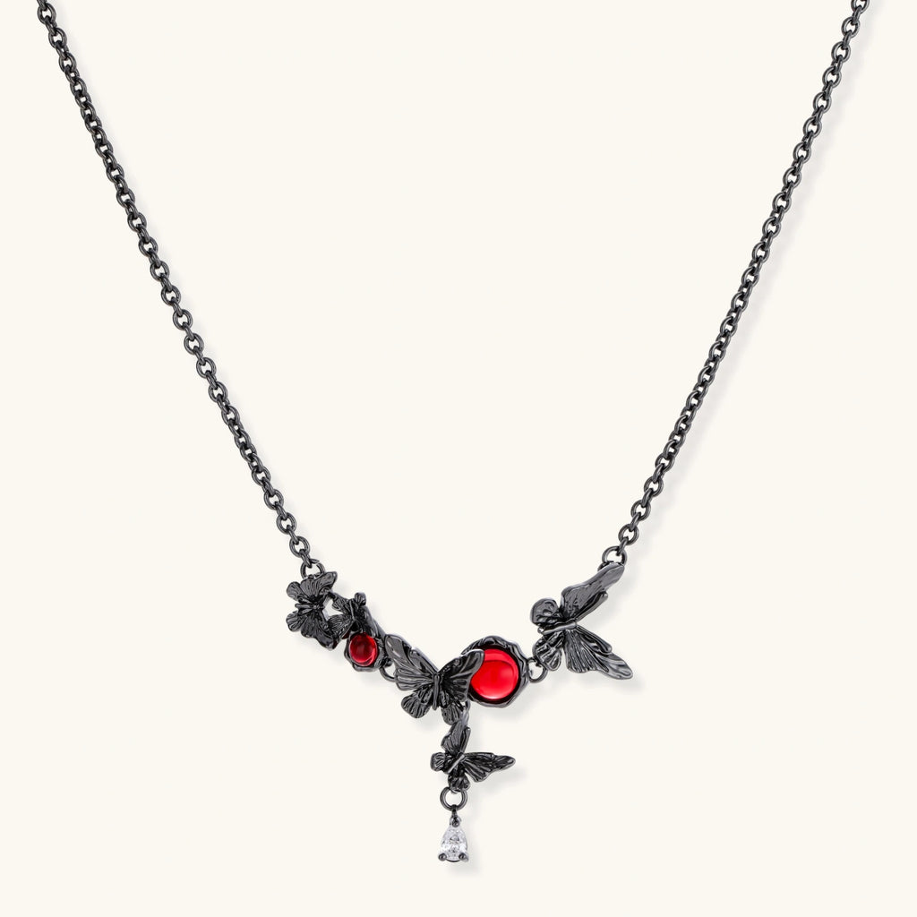 Dark oxidized metal necklace featuring red resin stones set in decorative leaf vine design with crystal drop pendant.