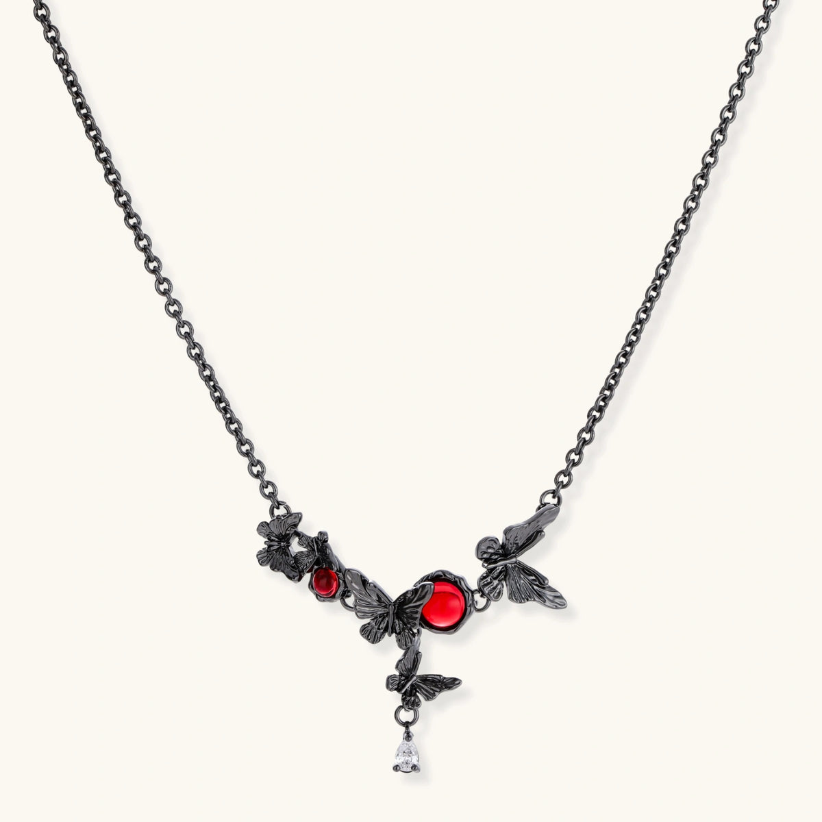 Dark oxidized metal necklace featuring red resin stones set in decorative leaf vine design with crystal drop pendant.