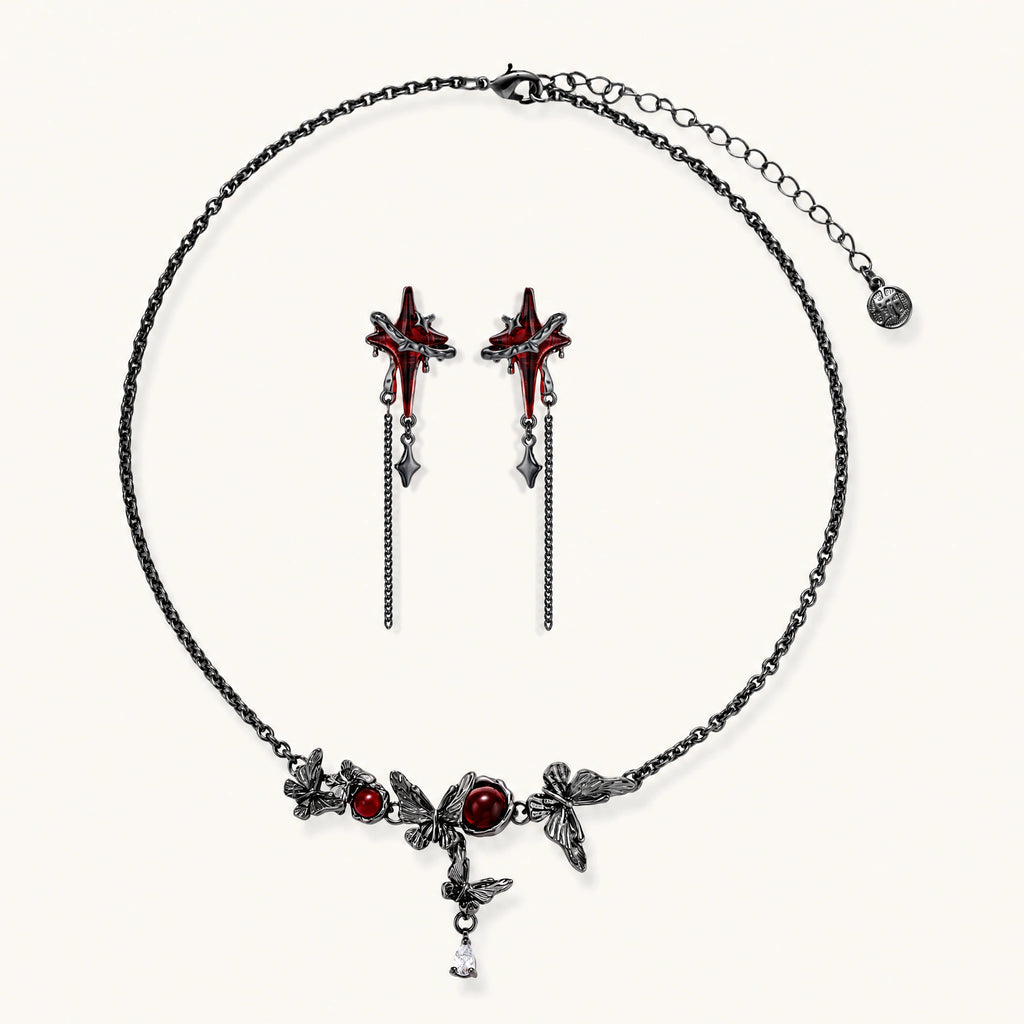 Gothic jewelry set with red resin cross pendants wrapped in dark metal chains on cream background.