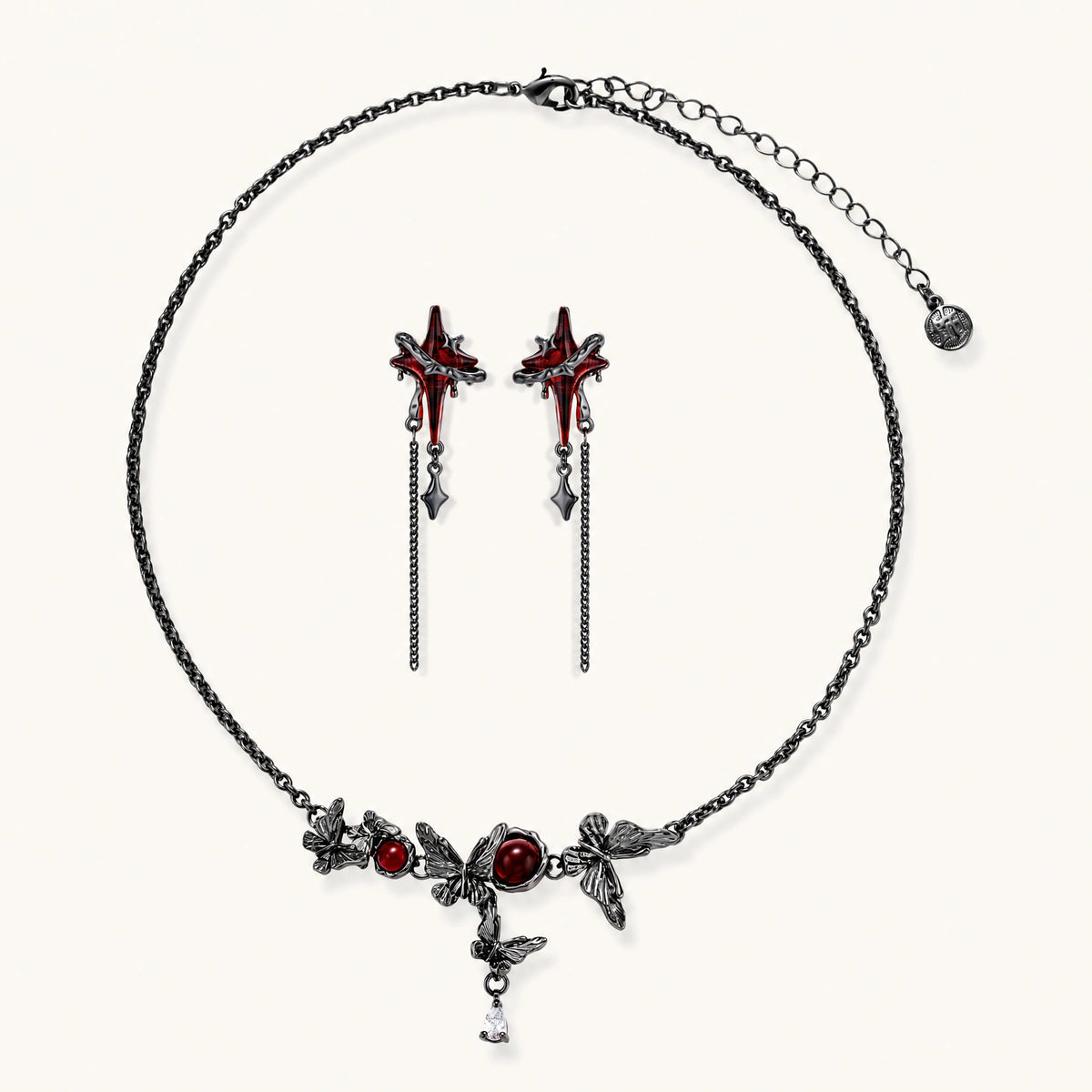 Gothic jewelry set with red resin cross pendants wrapped in dark metal chains on cream background.