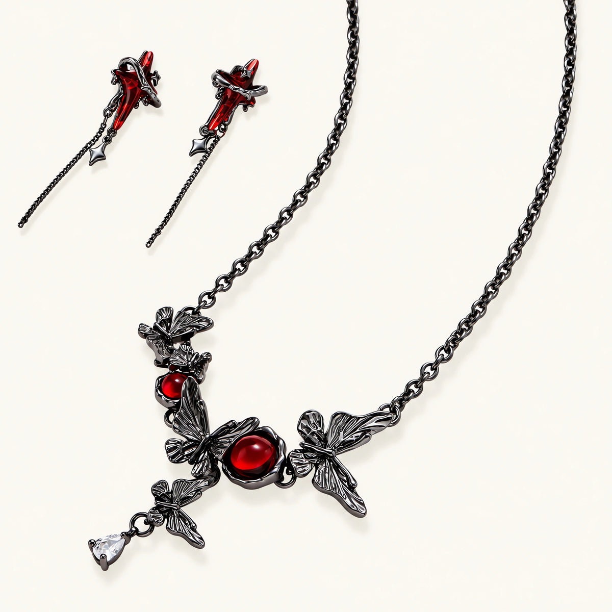 Gothic jewelry set with red resin cross pendants wrapped in dark metal chains on cream background.